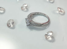 Load image into Gallery viewer, The two lines feature a row of brilliant cubic zirconia stones, radiating a stunning light comparable to diamonds. Connecting them is a large heart-shaped head, made from a large and reflective cubic zirconia. Hand-polished to perfection, you will love wearing this ring on its own or stacking it with other pieces to make the look more unique. Material: 925 Sterling Silver, Cubic Zirconia Design: Heart Weight: 2.6g