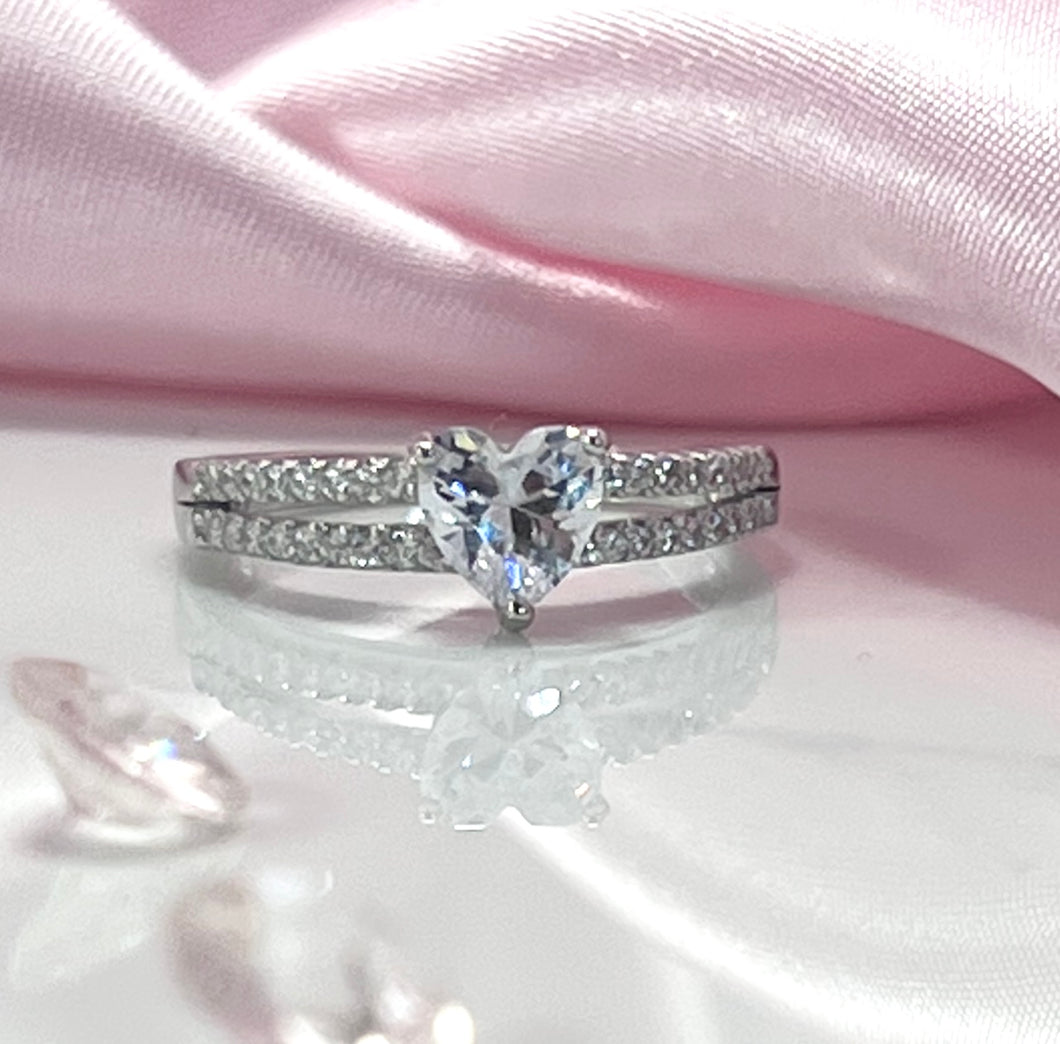 The two lines feature a row of brilliant cubic zirconia stones, radiating a stunning light comparable to diamonds. Connecting them is a large heart-shaped head, made from a large and reflective cubic zirconia. Hand-polished to perfection, you will love wearing this ring on its own or stacking it with other pieces to make the look more unique.  Material: 925 Sterling Silver, Cubic Zirconia  Design: Heart  Weight: 2.6g