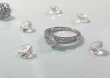 Load image into Gallery viewer, The two lines feature a row of brilliant cubic zirconia stones, radiating a stunning light comparable to diamonds. Connecting them is a large heart-shaped head, made from a large and reflective cubic zirconia. Hand-polished to perfection, you will love wearing this ring on its own or stacking it with other pieces to make the look more unique.  Material: 925 Sterling Silver, Cubic Zirconia  Design: Heart  Weight: 2.6g
