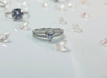 Load image into Gallery viewer, The two lines feature a row of brilliant cubic zirconia stones, radiating a stunning light comparable to diamonds. Connecting them is a large heart-shaped head, made from a large and reflective cubic zirconia. Hand-polished to perfection, you will love wearing this ring on its own or stacking it with other pieces to make the look more unique.  Material: 925 Sterling Silver, Cubic Zirconia  Design: Heart  Weight: 2.6g
